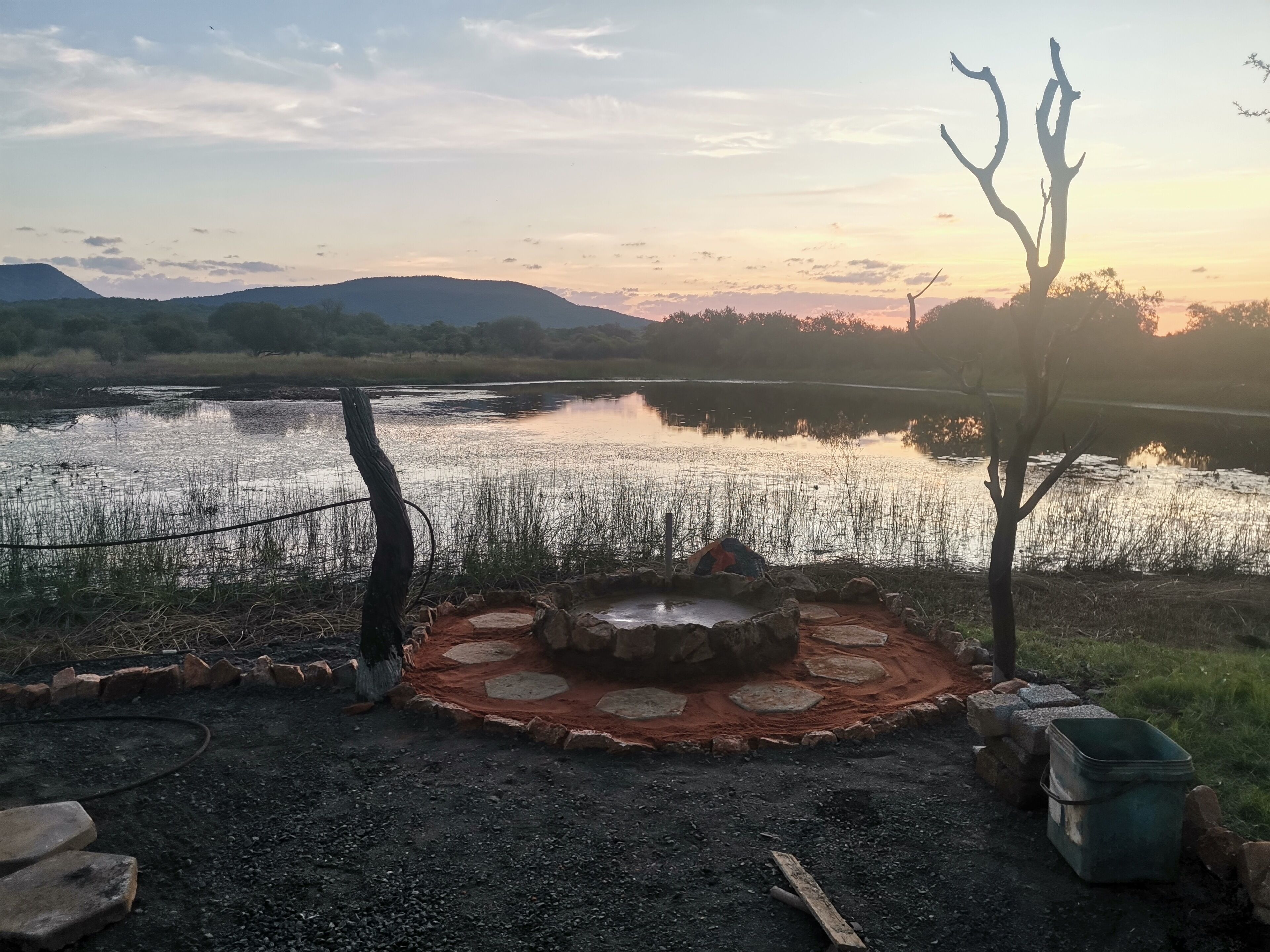 Een camping met een vuurkorf, een tent en uitzicht op een meer en bergen.