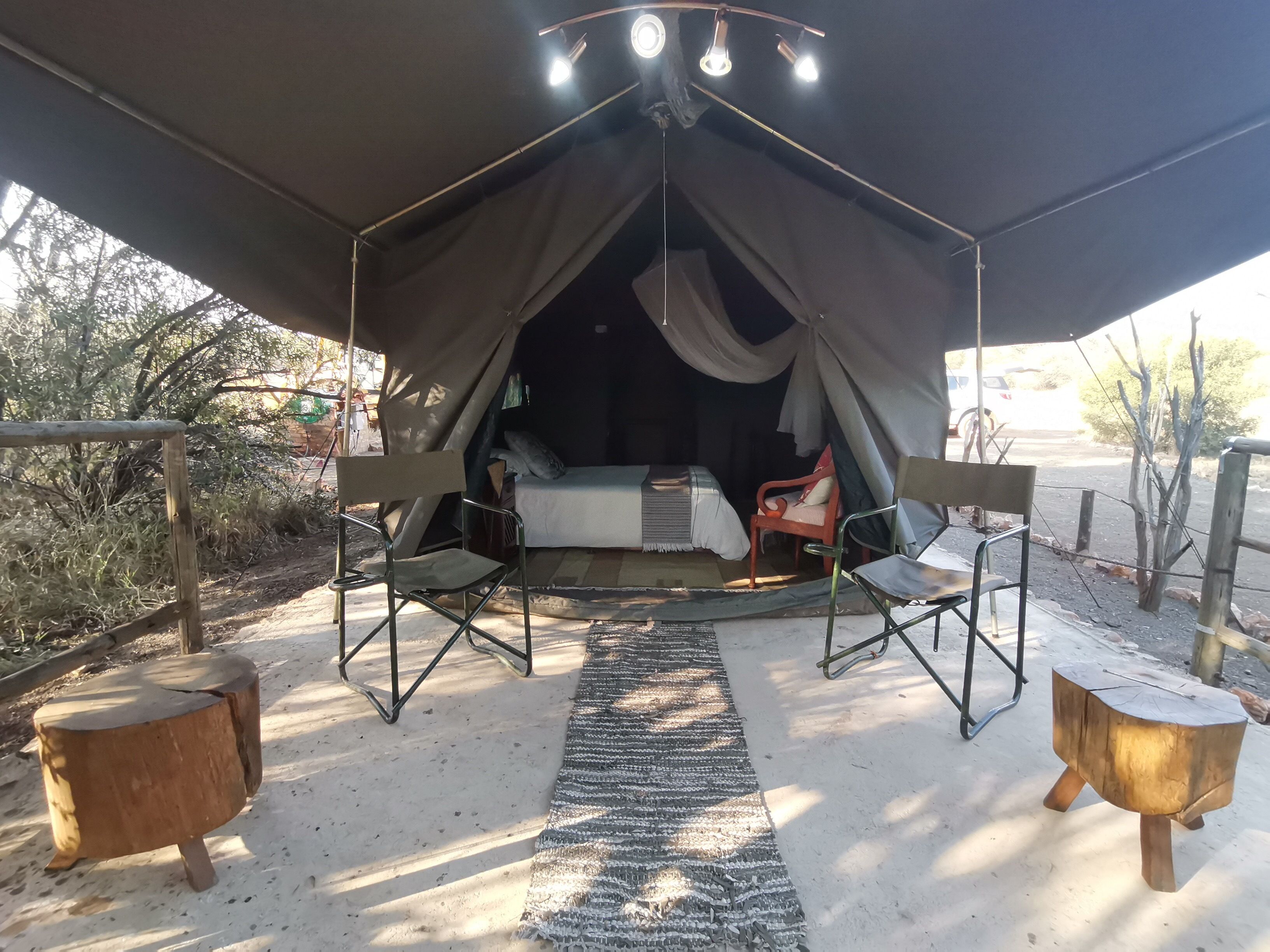 A tented accommodation with a bed, two chairs, and a small table.