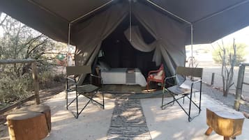 A tented accommodation with a bed, two chairs, and a small table.
