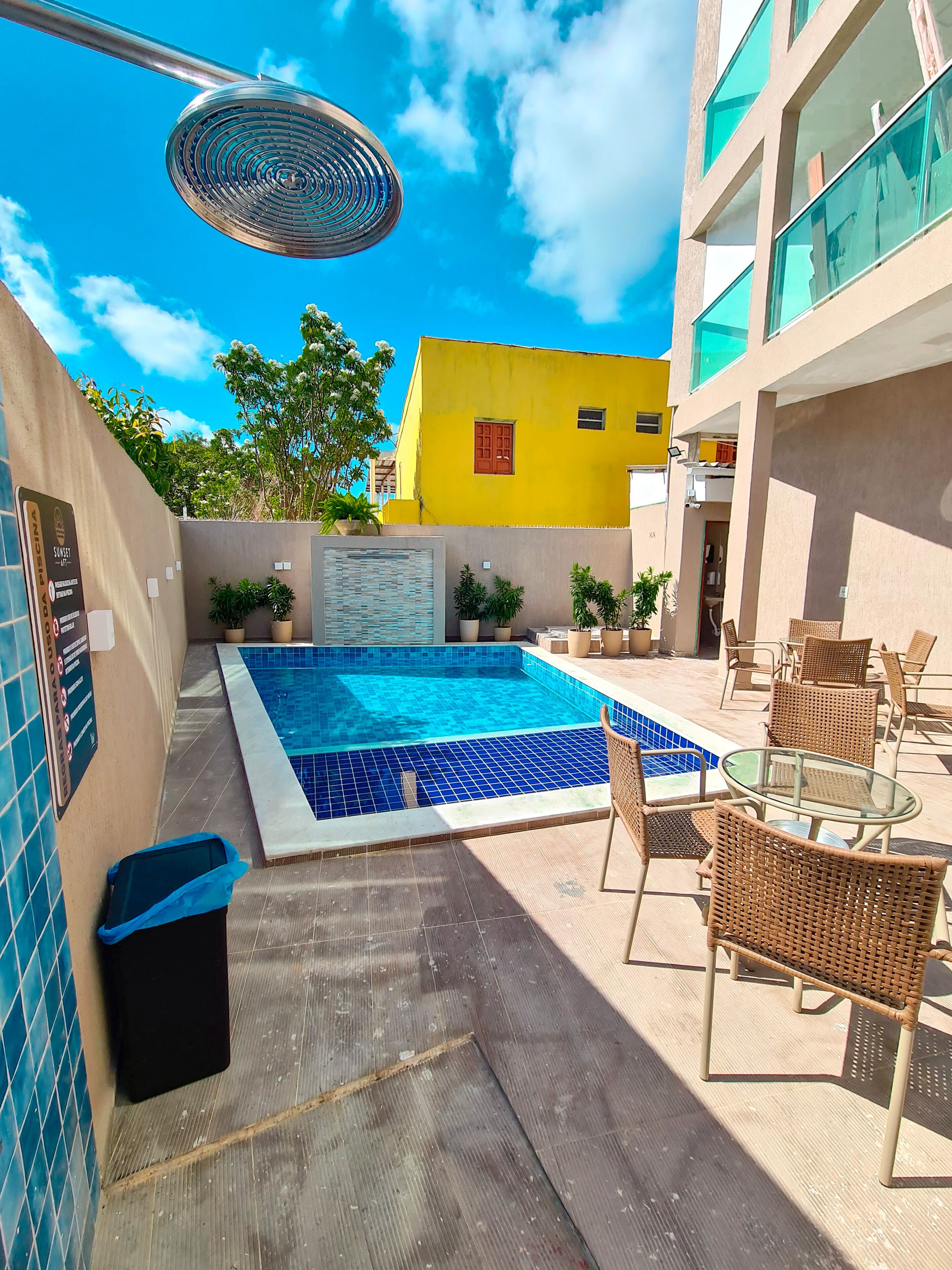 A rooftop pool area with a blue-tiled pool, wicker furniture, and potted plants.