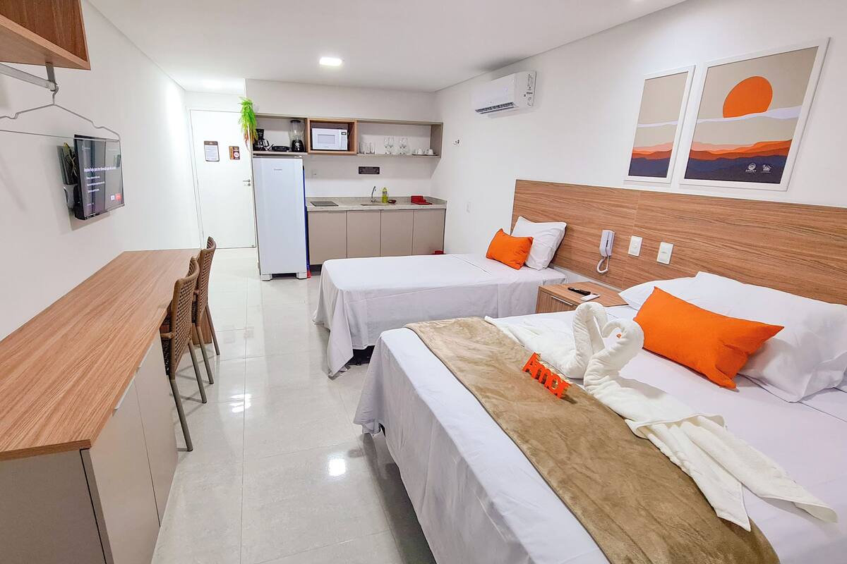 Habitación de hotel con dos camas, un escritorio de madera, kitchenette y vistas al atardecer.