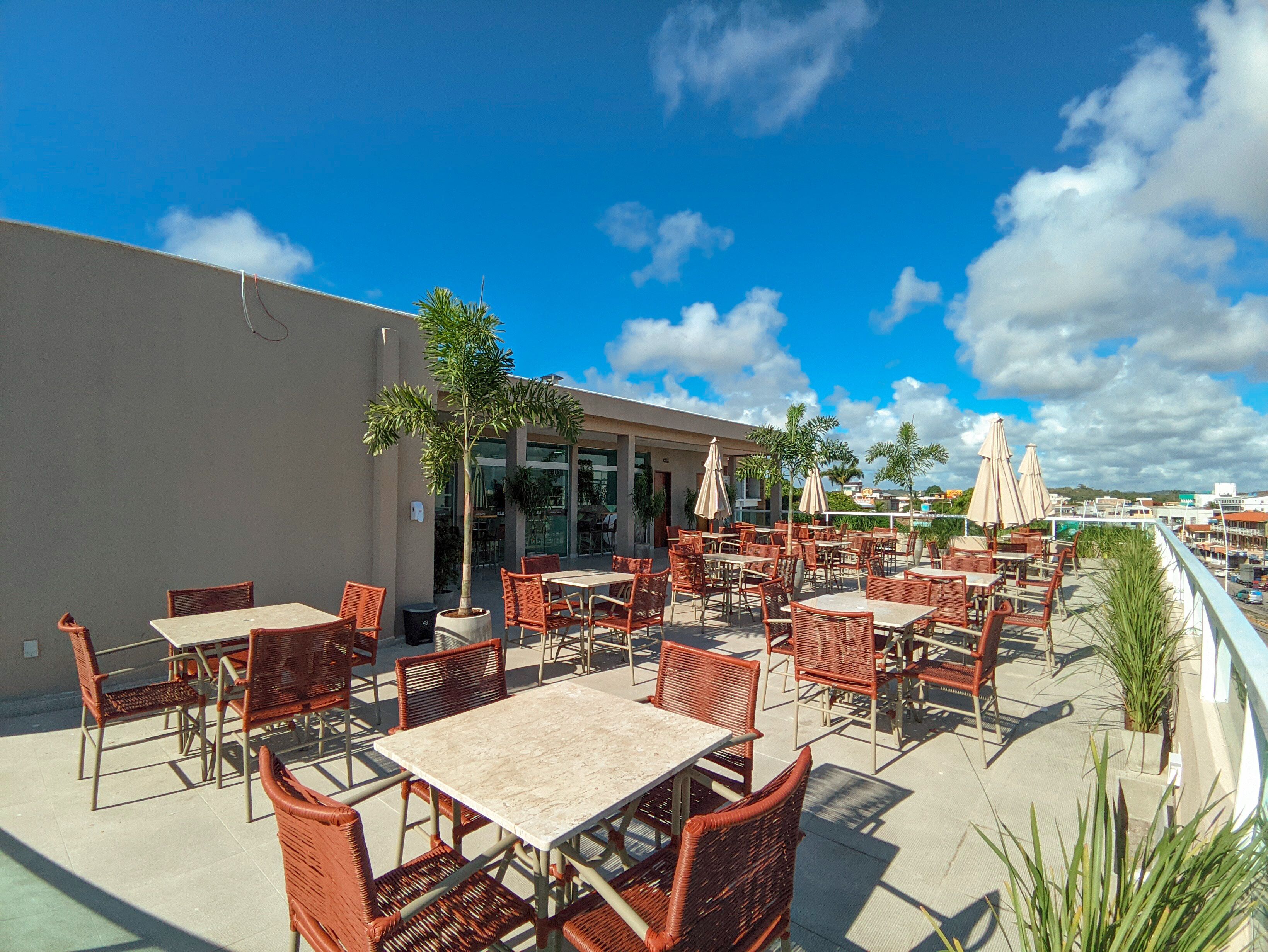 An outdoor patio with wicker tables and chairs, a palm tree, and a view of the city skyline.
