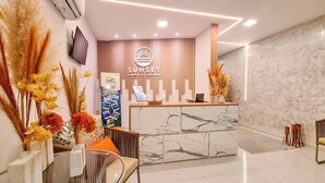 A reception area with a marble counter, a mounted TV, and a sign reading "SUNSET AFT". - Sunset by AFT - Porto de Galinhas (Ipojuca)