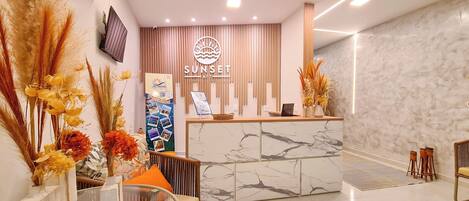 A reception area with a marble counter, a mounted TV, and a sign reading "SUNSET AFT".