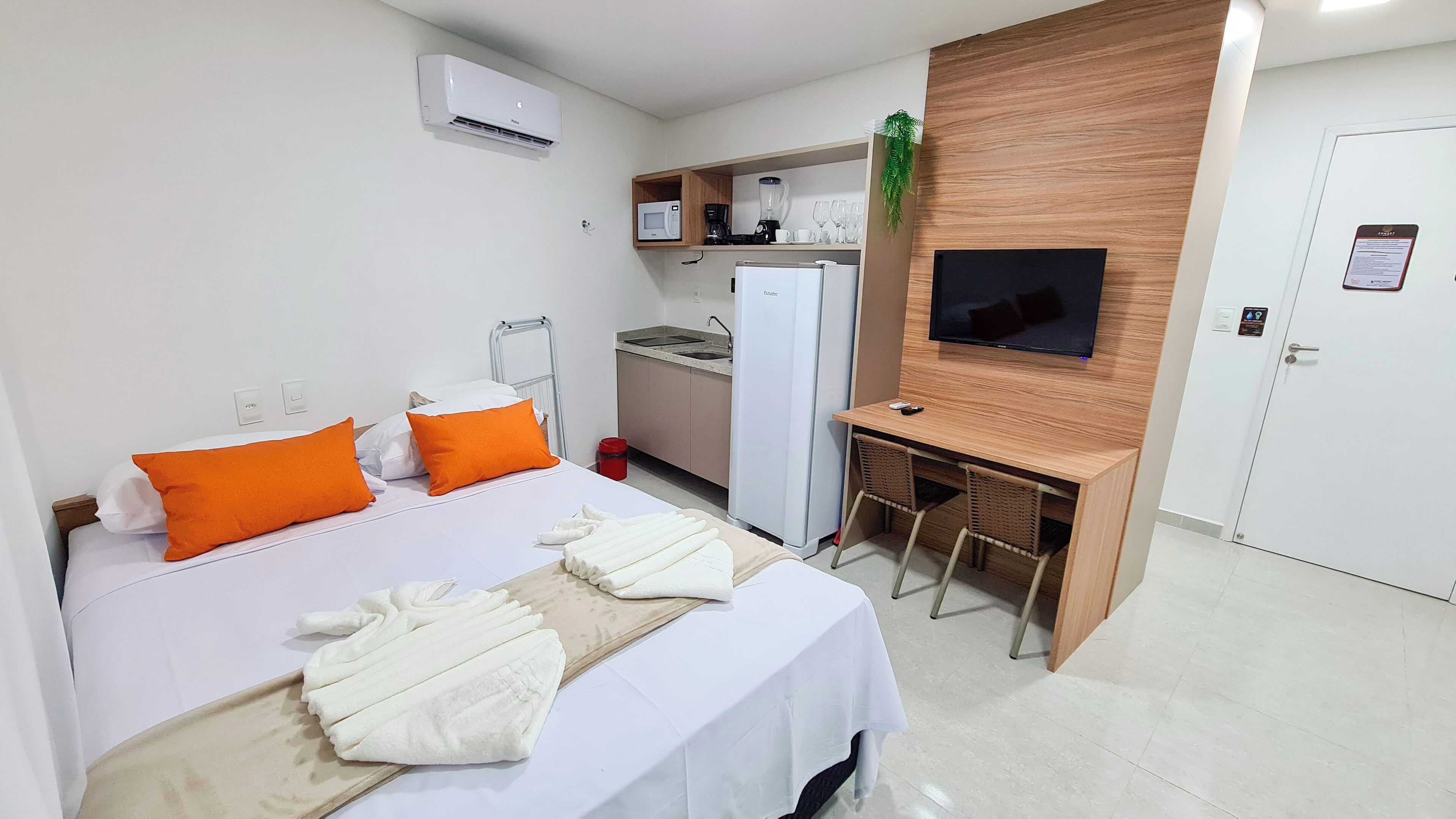 A hotel room with a bed, a desk, a TV, a microwave, a refrigerator, and a small kitchenette.