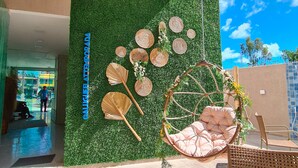 A modern outdoor seating area with wicker chairs and a hanging chair, a green wall with decorative elements, and a clear blue sky in the background. - Sunset by AFT - Porto de Galinhas (Ipojuca)