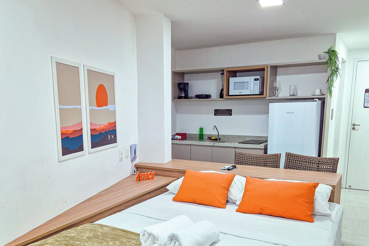 Una habitación de hotel con una cama, cabecera de madera, dos almohadas, una mesita de noche, una ventana y un televisor montado en la pared, además de microondas, refrigerador y lavamanos.