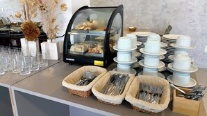 A buffet setup with a glass display case, stacked plates, bowls, and utensils. - Sunset by AFT - Porto de Galinhas (Ipojuca)