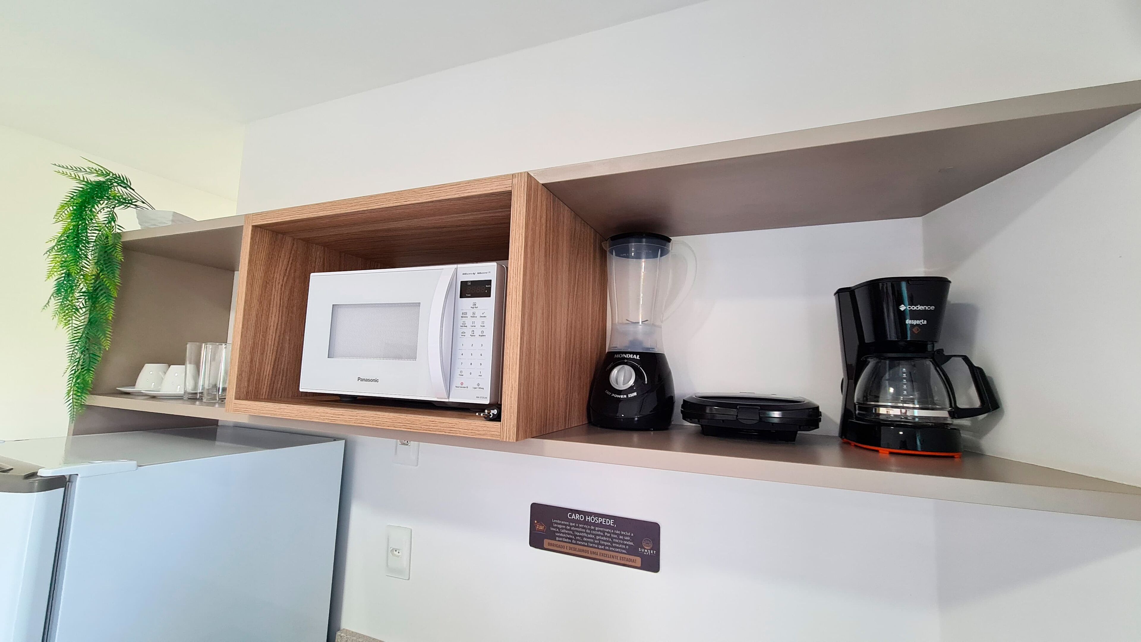 A kitchen with a microwave, blender, and coffee maker on a shelf.