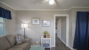 Un salon avec un canapé, une table basse, une lampe et une petite table d’appoint ornée de plantes. Un couloir mène à une autre pièce.