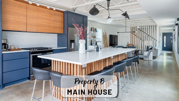 A modern kitchen with a central island, bar stools, and a dining area with a staircase leading to another level. - Contemporary East Austin Home + Separate Backyard Loft on Fenced-In Property (Austin)