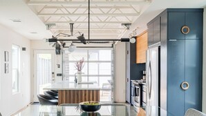 A modern kitchen with a glass dining table, two grey chairs, and a blue cabinet with a wooden handle. - Contemporary East Austin Home + Separate Backyard Loft on Fenced-In Property (Austin)