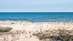 Ein Strand mit einem sandigen Pfad, der zum Wasser führt, einem Zelt und vereinzelter Vegetation.