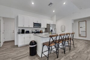 A modern kitchen with white cabinetry, a central island with bar stools, and a microwave.