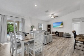 A spacious living area with a dining table, chairs, a sofa, a TV, and a ceiling fan.