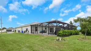 A residential house with a covered patio, a garage, and a well-maintained lawn. - New Build W/ Heated Pool! Perfect for 2 families! (Cape Coral)