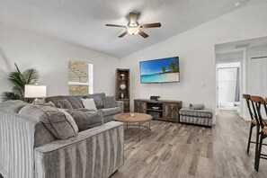A living room with a sectional sofa, a coffee table, a TV, and a ceiling fan.