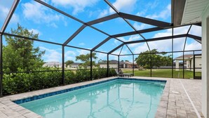 A swimming pool with a covered area, surrounded by a brick patio and a metal fence. - New Build W/ Heated Pool! Perfect for 2 families! (Cape Coral)