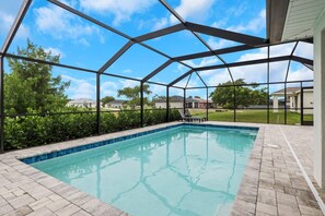 A swimming pool with a covered area, surrounded by a brick patio and a metal fence.