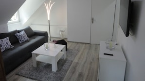Ein modernes Wohnzimmer mit grauem Sofa, weißem Couchtisch und einem an der Wand befestigten Flachbildfernseher.