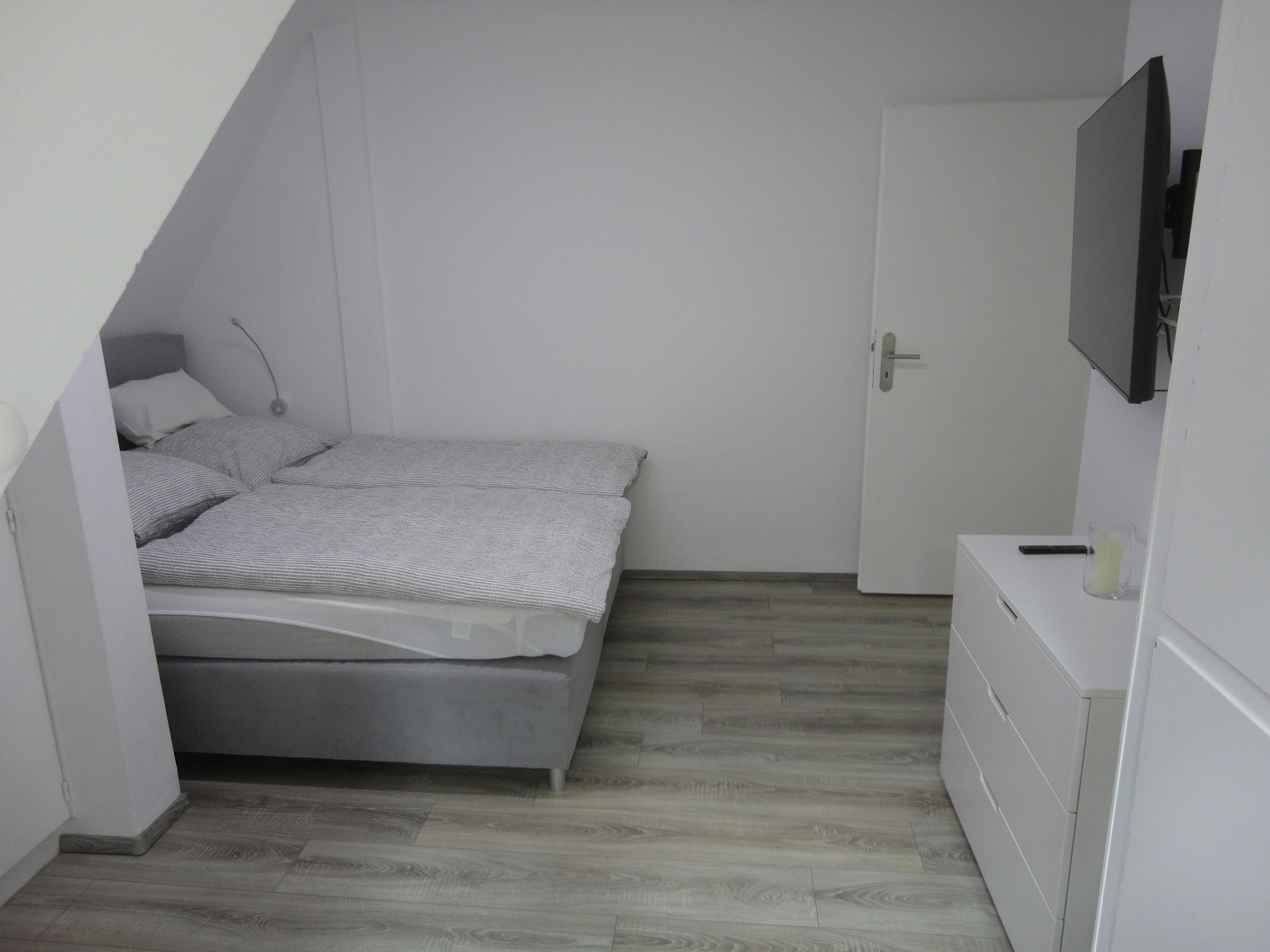 Un dormitorio pequeño y moderno con una cama, un aparador y un televisor en la pared.