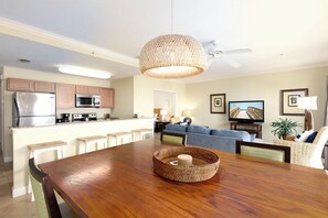 A modern kitchen with stainless steel appliances, a dining area with a wooden table, and a living room with a sofa and television.