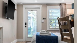 Une chambre d’hôtel avec un lit, une chaise, un téléviseur fixé au mur et une fenêtre avec des stores.