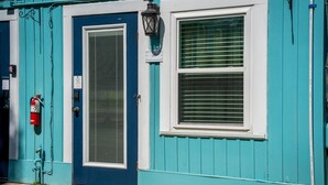 Un bâtiment de couleur bleu-vert avec une porte bleue, une fenêtre avec des stores, un extincteur et une lanterne noire.