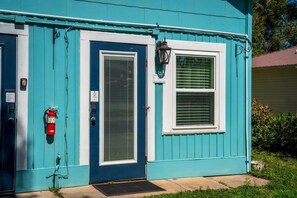A teal building with a blue door, a window with blinds, a fire extinguisher, and a small outdoor light fixture.