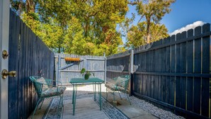 Une terrasse avec une table et des chaises, entourée d’une clôture en bois et d’arbres.