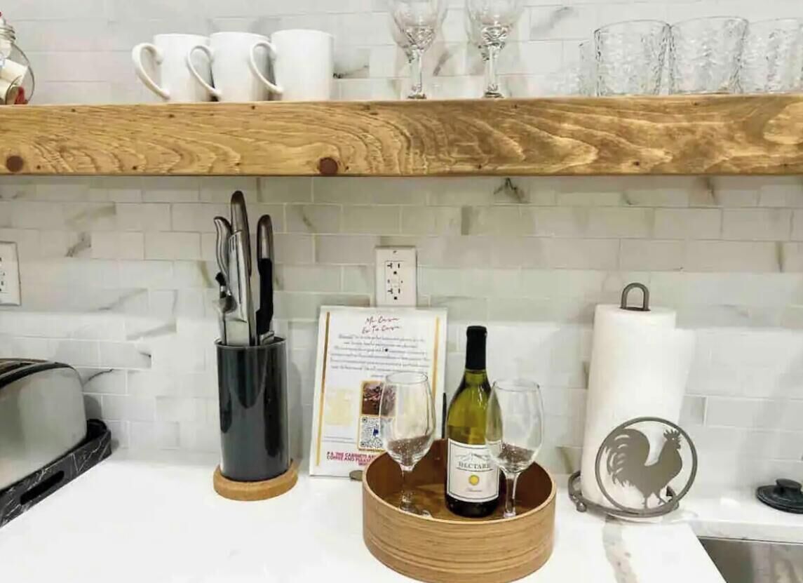 A kitchen counter with a wooden tray holding a bottle of wine and two glasses, a set of knives, a corkscrew, and a menu.