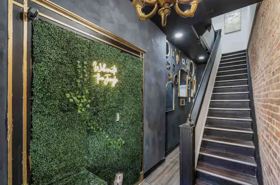 A staircase with a brick wall on one side and a green wall with a neon sign on the other.