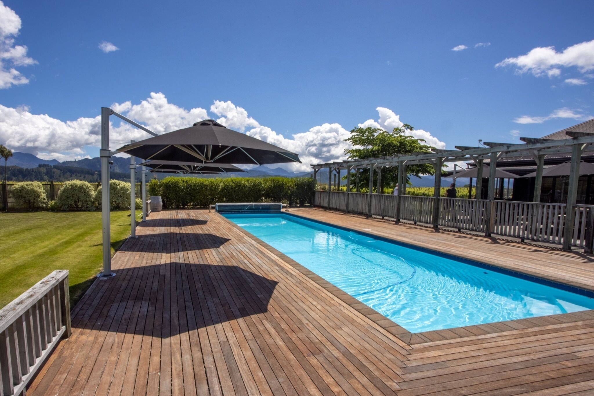 Une piscine avec une terrasse en bois, des parasols et une pergola.