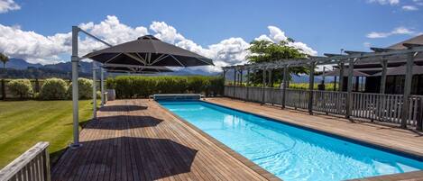 Une piscine avec une terrasse en bois, des parasols et une pergola.