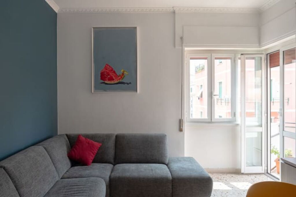 A modern living room with a grey sofa, a red pillow, and a framed artwork on the wall.