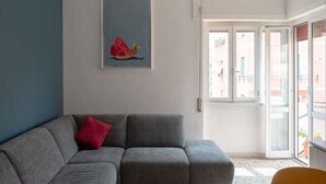 Un salon moderne avec un canapé gris, un coussin rouge et une œuvre d’art encadrée accrochée au mur.