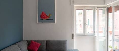 A modern living room with a grey sofa, a red pillow, and a framed artwork on the wall.