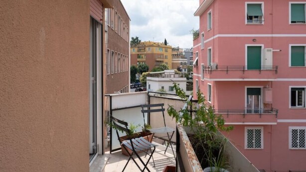 Un balcon avec une chaise et une petite table, donnant sur une rangée de bâtiments aux couleurs vives.