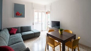 Un salon moderne avec un canapé gris, une table à manger avec des chaises jaunes, un téléviseur à écran plat et un tableau accroché au mur.
