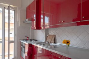 A kitchen with red cabinets, a white countertop, and a vase with sunflowers. - In the heart of Monteverde (Roma)