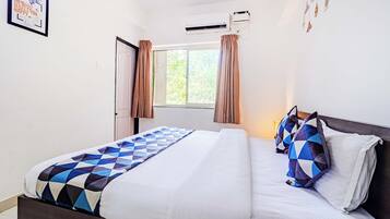 A hotel room with a bed, a window with curtains, an air conditioning unit, and a motivational poster on the wall.