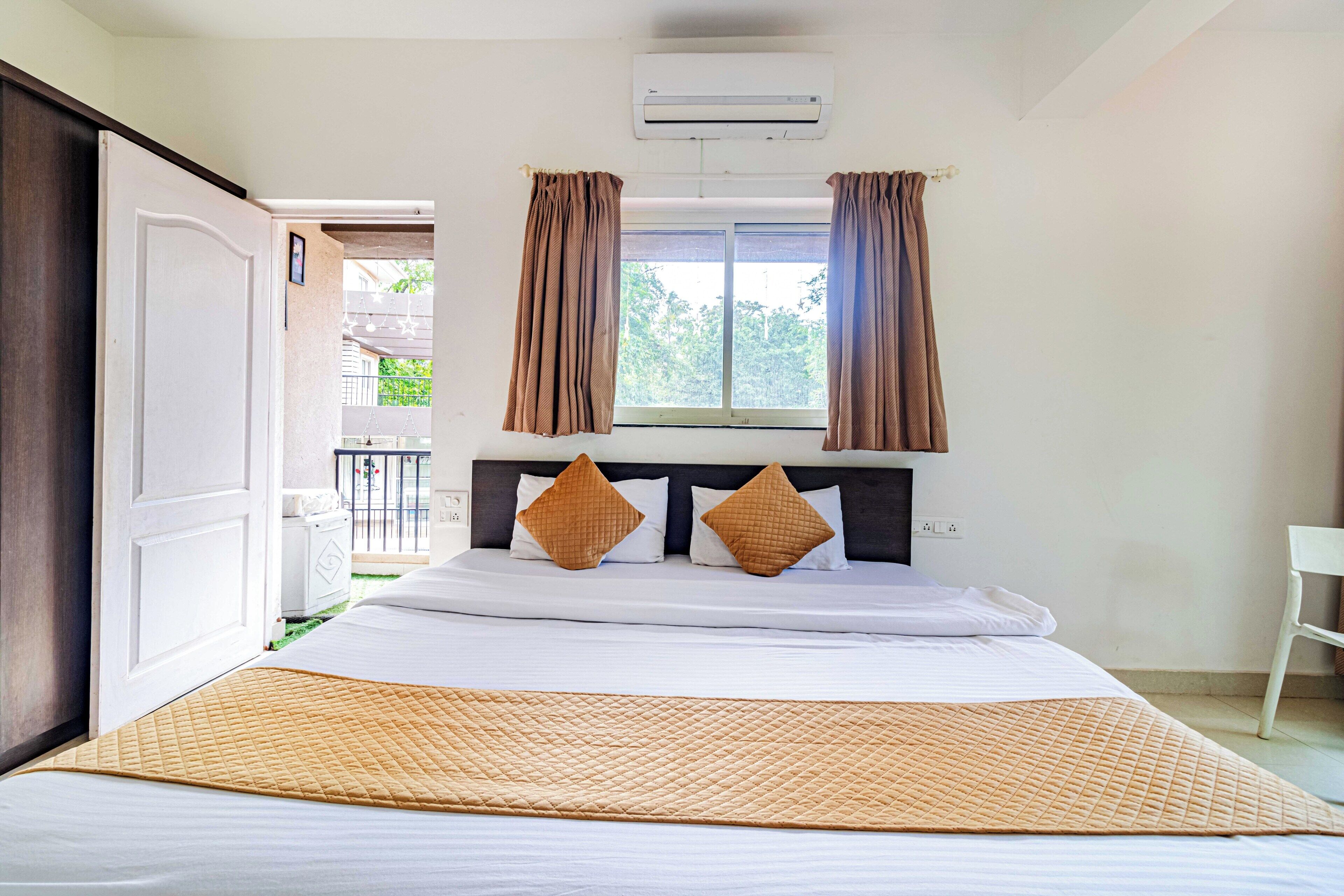 A hotel room with a bed, a window with curtains, an air conditioning unit, and a view of the outside balcony.