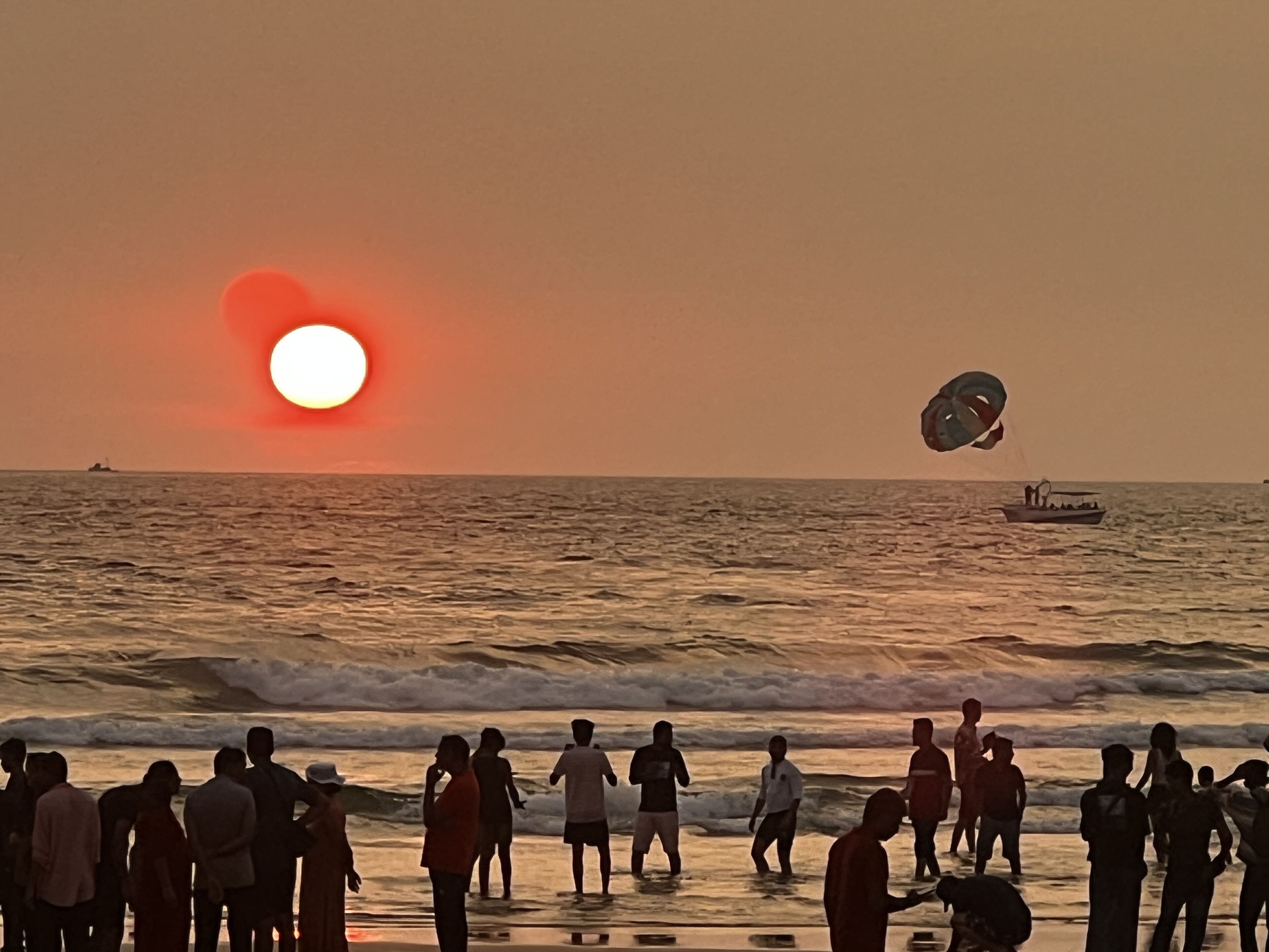 A beach scene with people and a boat in the water during sunset.