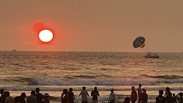 A beach scene with people and a boat in the water during sunset.