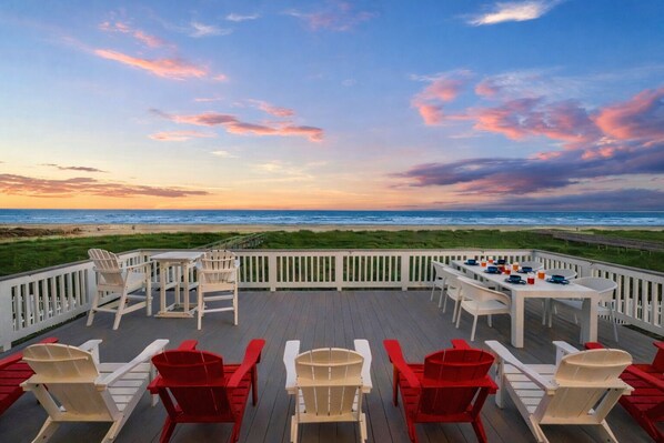 Une terrasse avec des sièges extérieurs et une vue sur la plage au coucher du soleil.