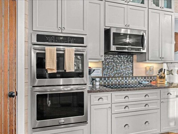 A kitchen with two stainless steel ovens, a microwave, and white cabinetry. - 2nd Row Beach 6BR | Sleeps 15 | Pointe West Amenities (Galveston)