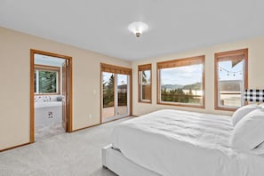 Un dormitorio con una cama grande, vistas al exterior a través de ventanas y una puerta corrediza que da a un balcón.