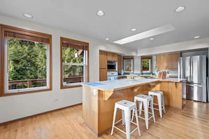 Una cocina moderna con armarios de madera, una isla central con taburetes y un refrigerador de acero inoxidable.
