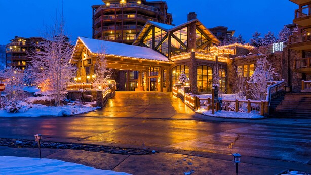 Un hôtel dont l’entrée est recouverte de neige, illuminée par des lumières chaleureuses, et dont l’imposant bâtiment s’étend sur plusieurs étages en arrière-plan.