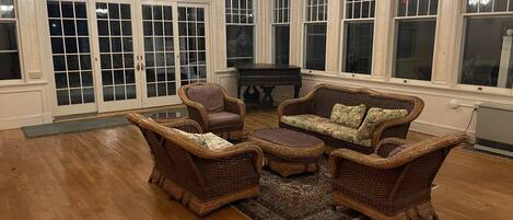 A spacious room with a piano, wicker furniture, large windows, and an exit sign.